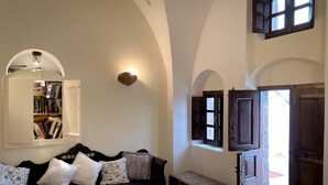 A cozy living room with a dark blue sofa, multiple pillows, a small wooden bench, and a bookshelf. - The Commander s House (Santorini)