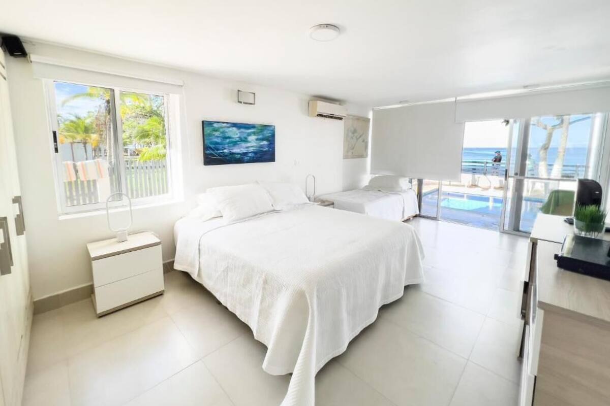 Un dormitorio con una cama grande, una mesita de noche, una ventana con vistas a palmeras y un cuadro en la pared.