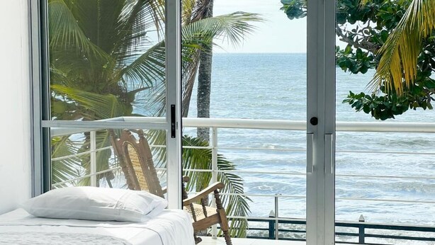 A bedroom with a bed, a rocking chair, and a view of the ocean through a sliding glass door. - Quinta del Mar El Francés (Tolu)
