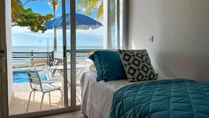 A bedroom with a view of a pool and palm trees, a bed with a teal comforter, and a patterned pillow. - Quinta del Mar El Francés (Tolu)