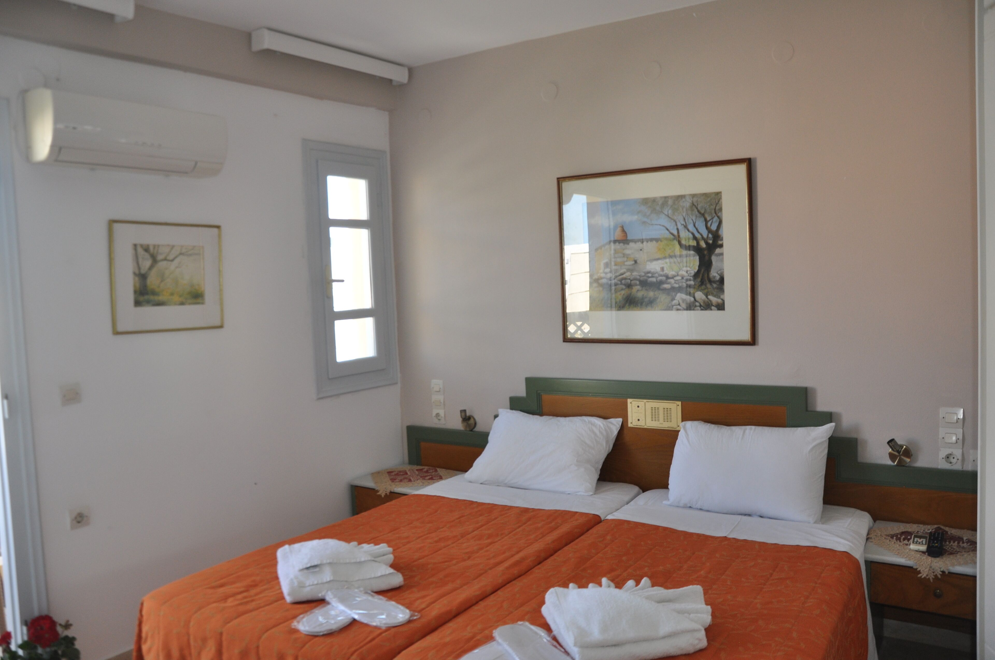 A double bed with an orange bedspread, two white pillows, and a framed landscape painting above it.