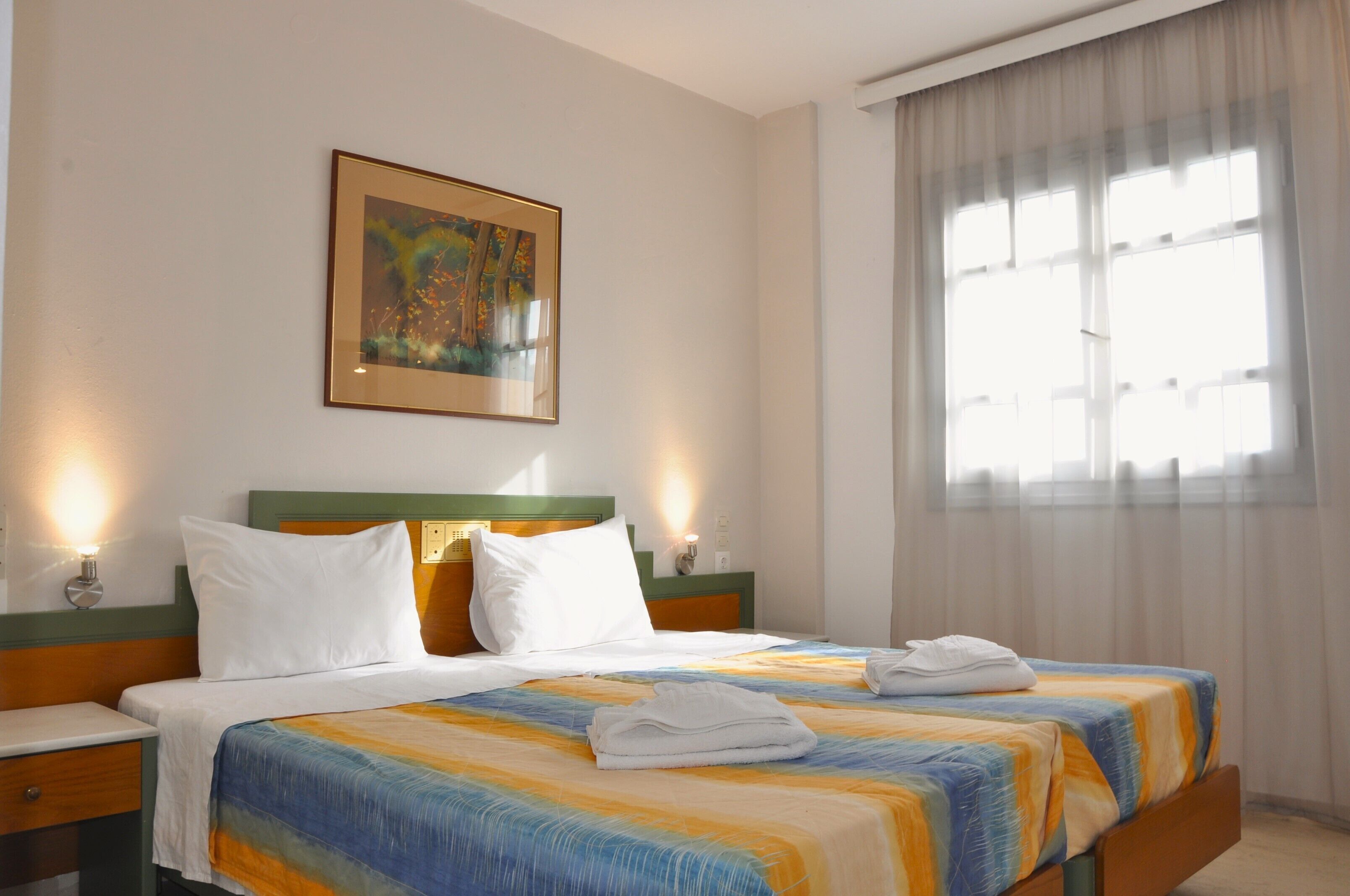 A hotel room with two beds, a painting on the wall, and a window with curtains.