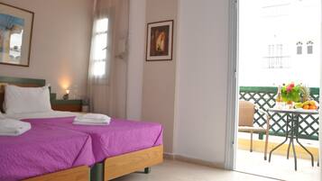 Habitación de hotel con cama, mesita de noche, un cuadro enmarco y balcón con mesa, silla y fruta.