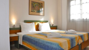 Una habitación de hotel con una cama, dos mesitas de noche, una lámpara de noche, un cuadro en la pared y una ventana con cortinas.