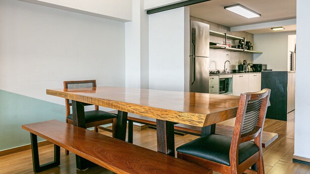 A modern dining area with a wooden table and chairs, a bench, and a kitchen in the background.