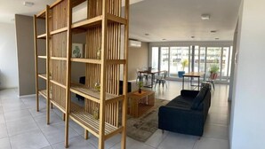A spacious living area with a large wooden bookshelf, a dark blue sofa, and a dining table with chairs.