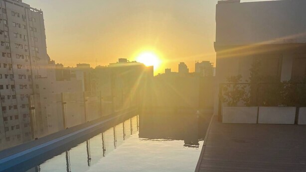 A rooftop pool with a clear view of the sunset over a cityscape.