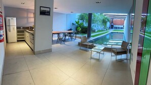 A modern kitchen with a refrigerator, a dining area with a table and chairs, and a view of a courtyard with a pool.