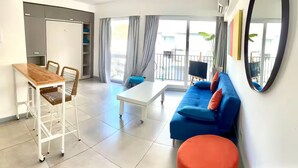A modern living room with a sofa, a table, and a chair. There is a balcony with a view outside.