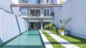 A modern building with a swimming pool, a covered outdoor area with seating, and a well-maintained lawn.