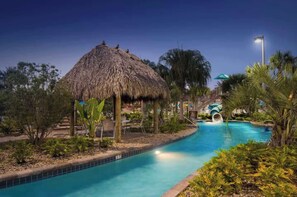 A pool area with a thatched structure, a slide, and surrounding tropical vegetation. - Luxury Resort Getaway | Disney Themed, Theater, Private Pool, Game Room & Sleeps 20! (Four Corners)