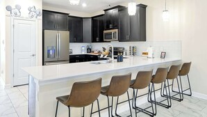 A modern kitchen with dark cabinets, stainless steel appliances, a white island with bar stools, and decorative Mickey Mouse wall art.