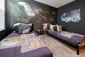A bedroom with two beds, Star Wars-themed wall art, and a Star Wars-themed bedspread.