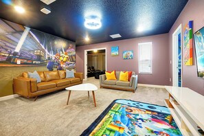 A room with a brown leather sofa, a white coffee table, a grey sofa with colorful cushions, a carpet with a colorful design, and a ceiling mural.