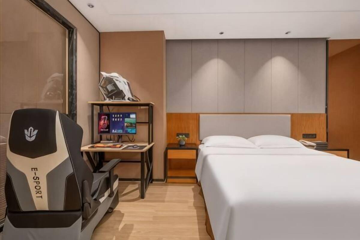 Una habitación de hotel moderna con una cama, un escritorio con computadora, una silla gamer y un televisor.
