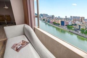 Una sala de estar moderna con un sofá frente a un ventanal que ofrece vistas a un paisaje urbano y un río.