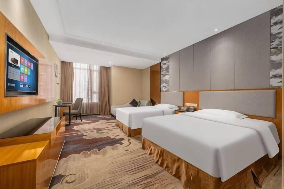 Habitación de hotel con dos camas, un escritorio, un televisor y un ventanal grande.