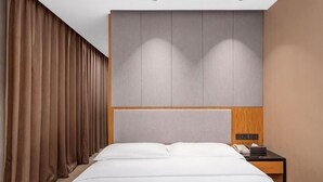 Una habitación de hotel con cama, mesita de noche, panel de pared y cortina.
