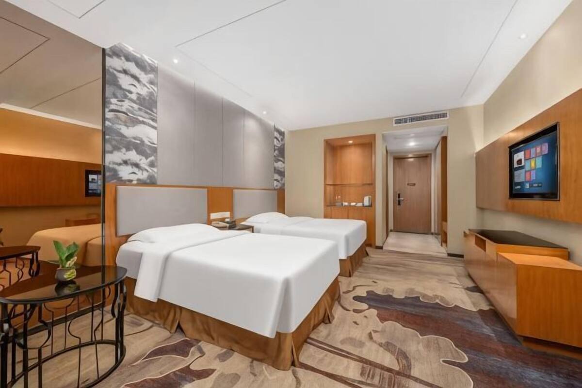 Habitación de hotel con dos camas, un escritorio, un televisor y una zona de recepción.