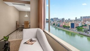 Habitación de hotel moderna con un ventanal grande, un sofá, una mesa con una planta y vistas a un paisaje urbano y un río.