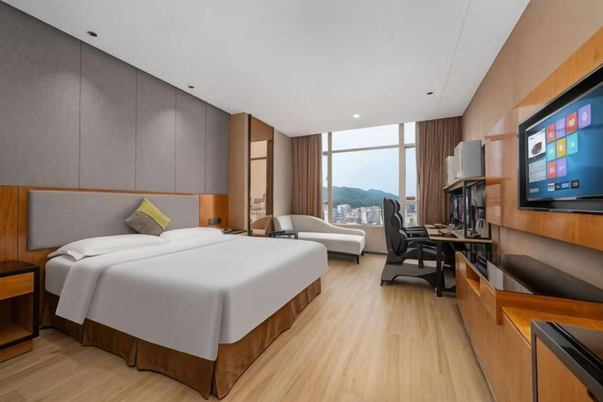 Habitación de hotel con una cama grande, un escritorio, una silla, televisión y vistas a la ciudad.