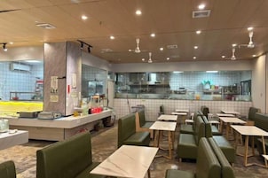 Interior de un restaurante con cabinas, mesas y una zona de cocina visible a través de un tabique de vidrio.
