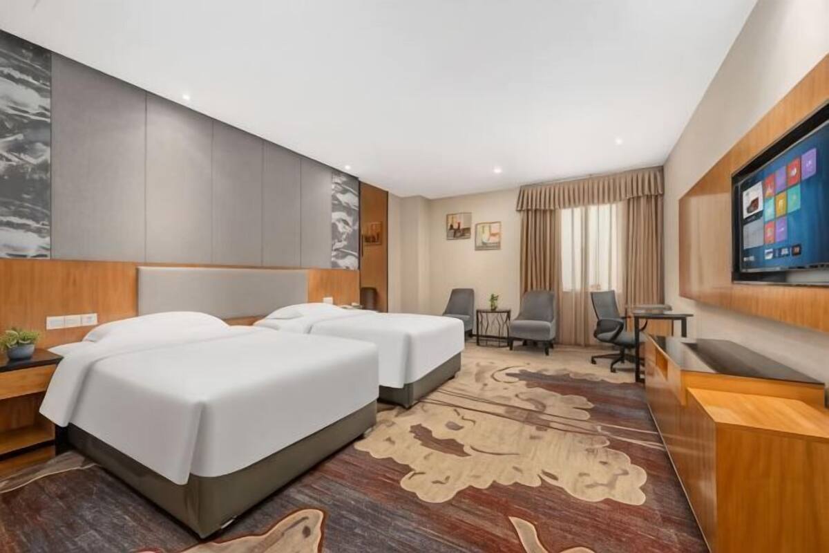 Habitación de hotel con dos camas, un escritorio, un televisor y un ventanal grande.