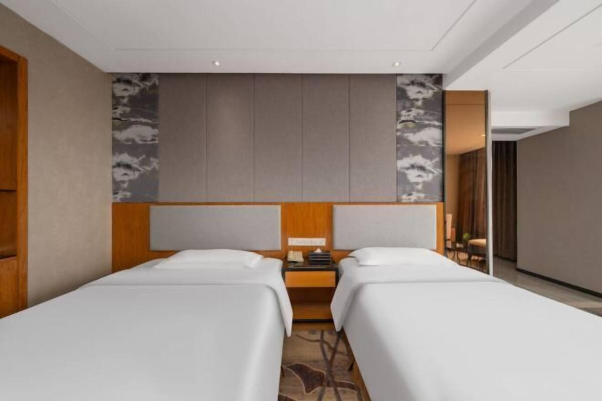 Habitación de hotel con dos camas individuales, cabecera de madera, mesita de noche y pared con diseño decorativo.