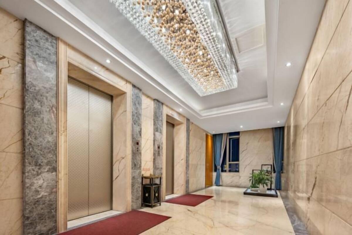 Un vestíbulo de hotel con paredes de mármol, una araña y alfombras rojas, además de una planta en maceta.