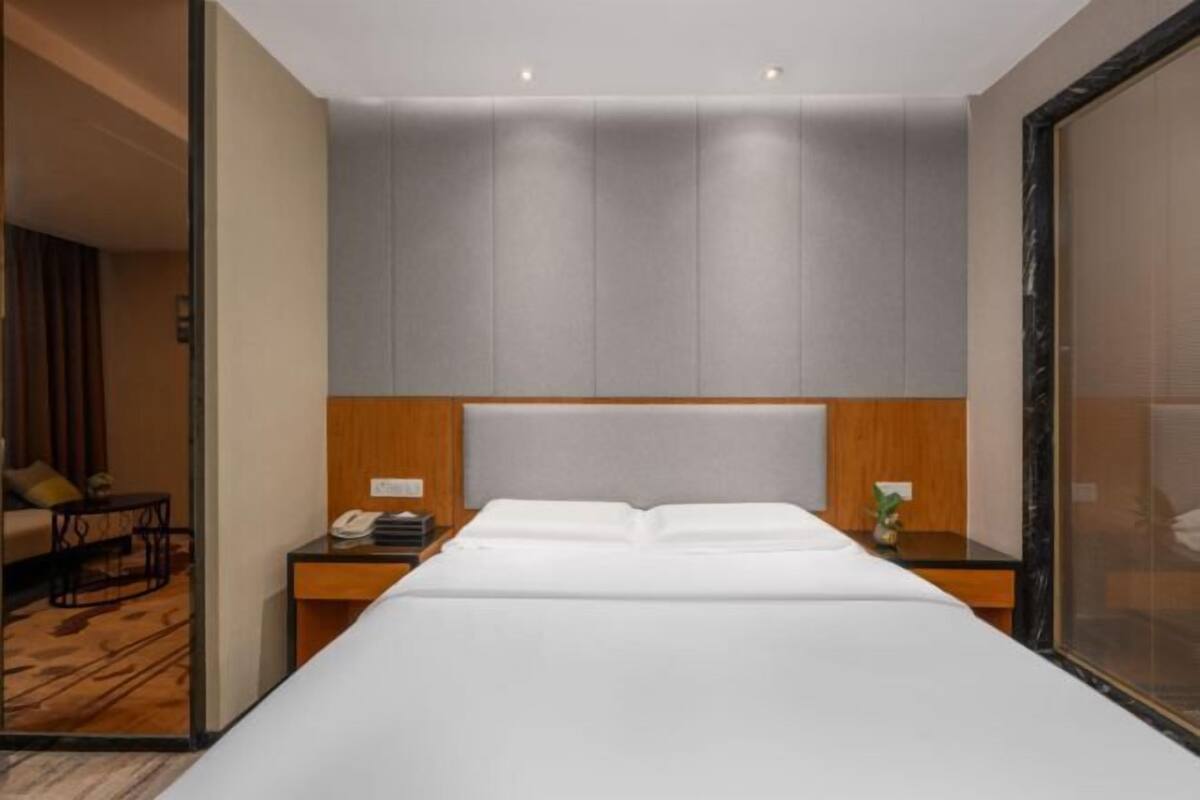 Una habitación de hotel moderna con una cama grande, una mesita de noche de madera, una pequeña mesa y un separador de vidrio.