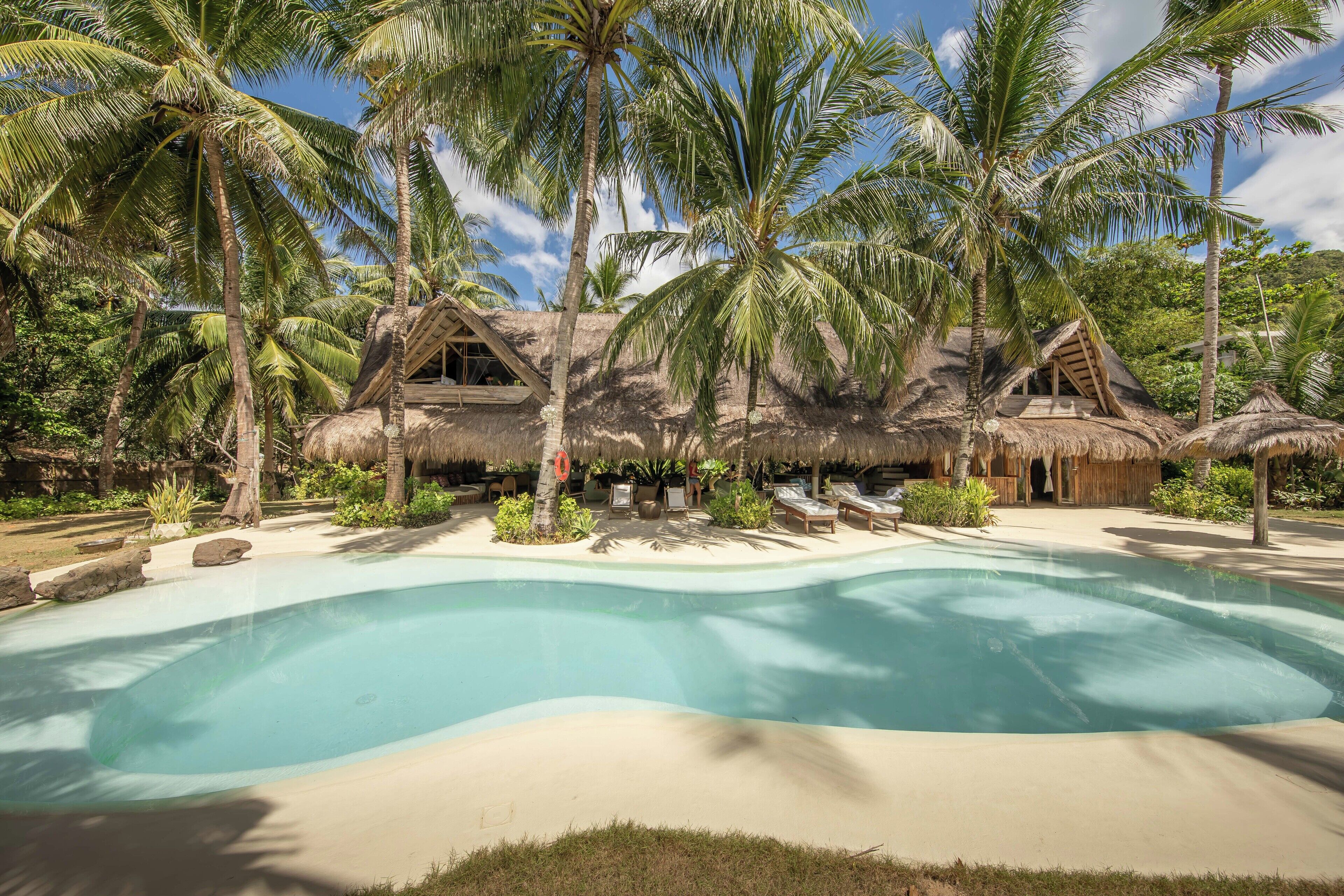 A resort with a large pool, palm trees, and thatched-roof huts.