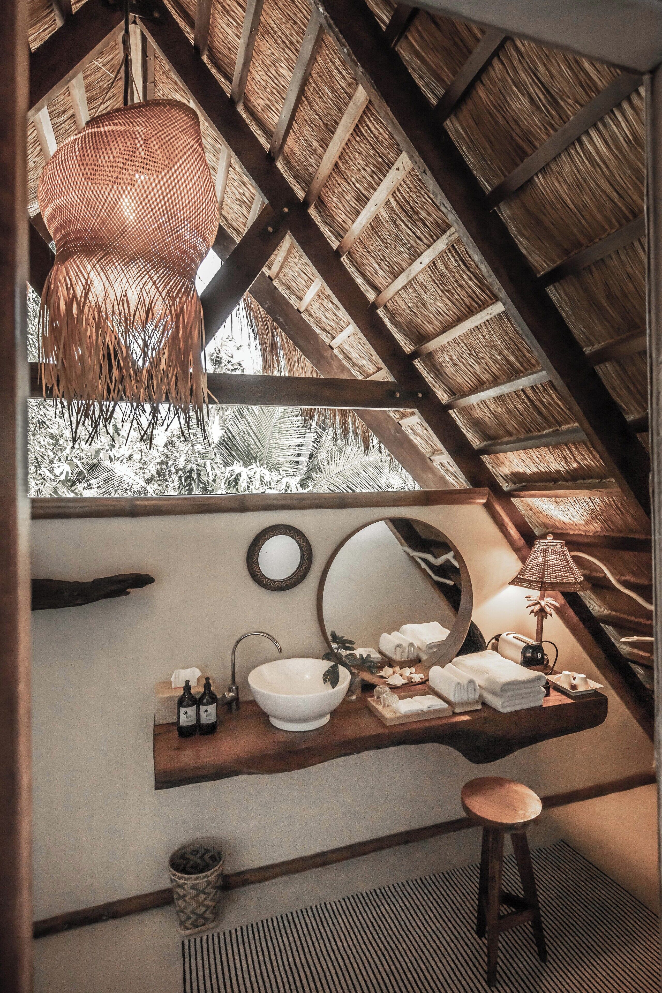 A bathroom with a wooden ceiling, a large mirror, a sink, and a hanging light fixture.