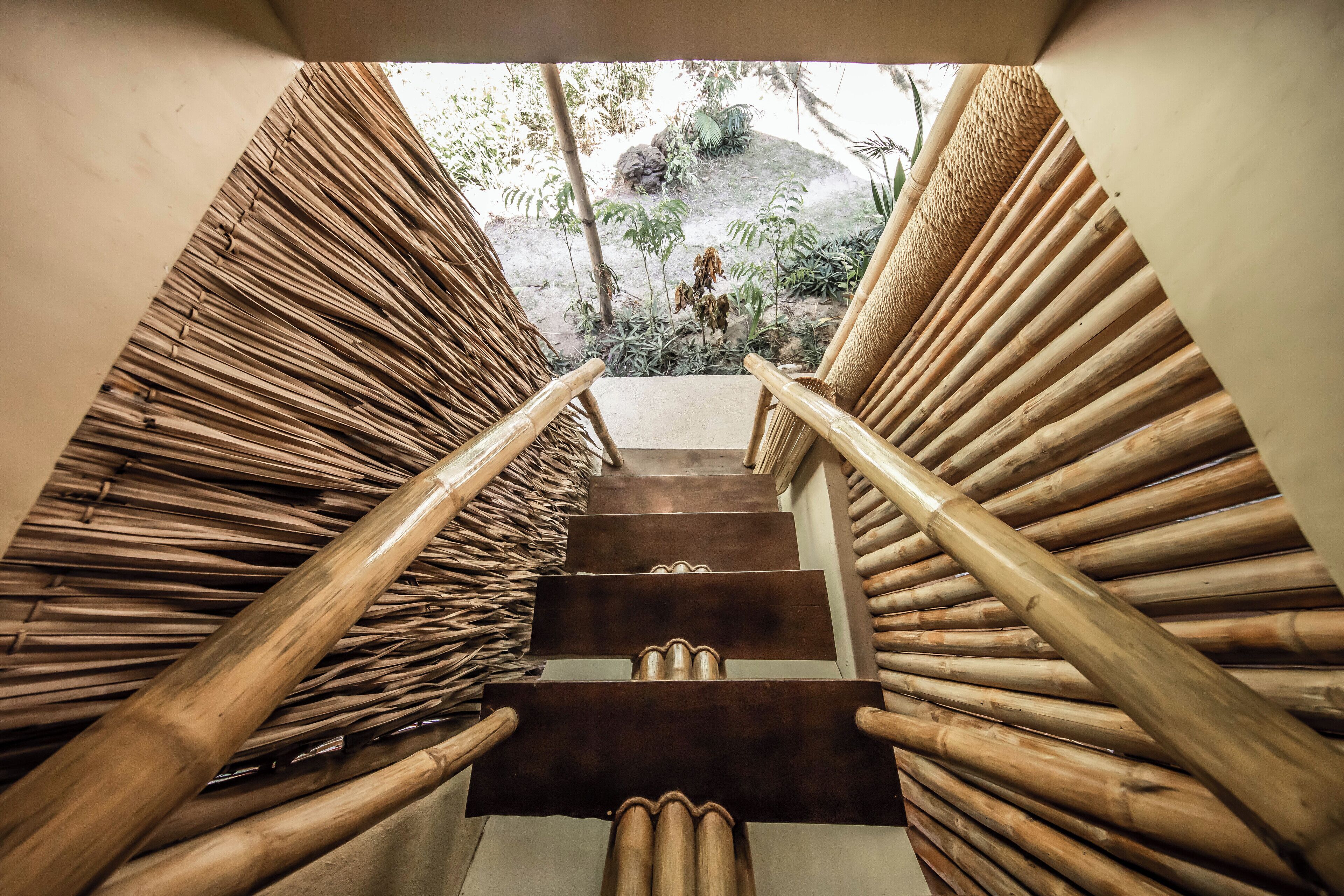 Una escalera con barandilla de diseño natural y tejido, que conduce a un espacio al aire libre con plantas y rocas.