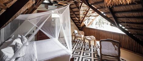 A high-ceilinged attic bedroom with a bed, a woven hanging light fixture, and a patterned rug.