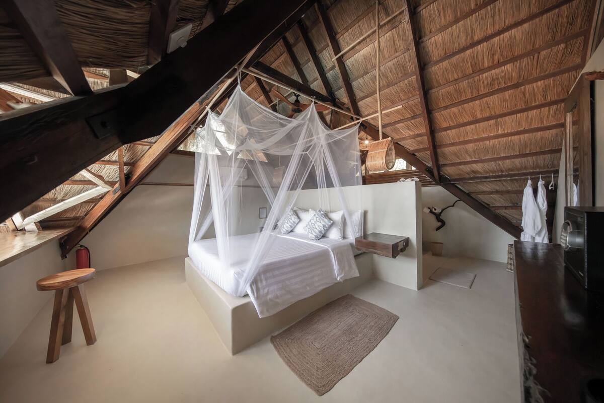 A bedroom with a canopy bed, a small stool, a bedside table, and a hanging chair.