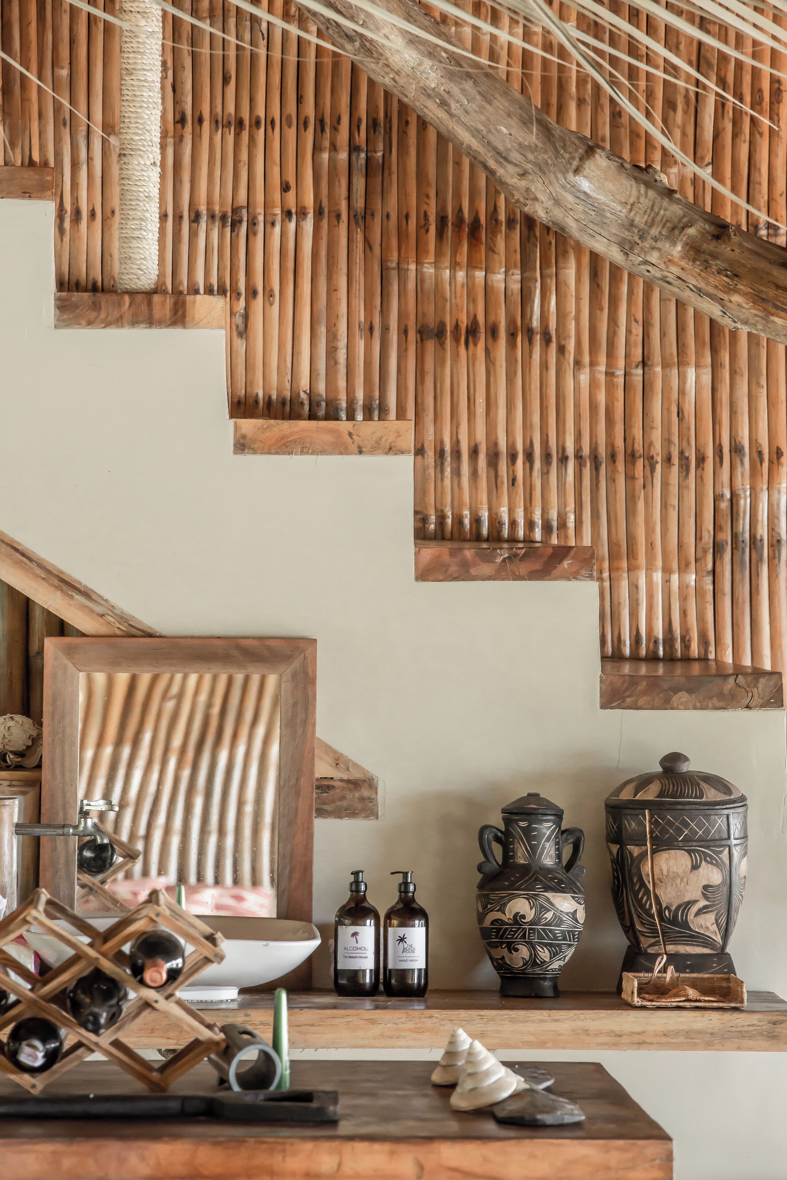 Un interior rústico con paneles de pared de bambú, una estantería de madera para vino, cerámica decorativa y un espejo.