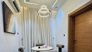 A dining area with a round table, four upholstered chairs, a hanging light fixture, and a wooden door. - Jayz Shortlet Apartment (Abuja)