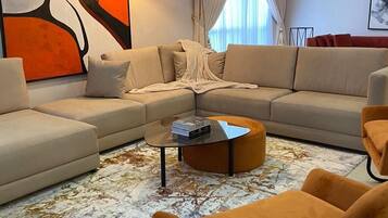 Ein modernes Wohnzimmer mit einer Eckcouch, einem runden Couchtisch und einem großen abstrakten Gemälde an der Wand.