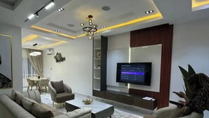 A modern living room with a sofa, armchairs, a coffee table, and a TV. - Jayz Shortlet Apartment (Abuja)