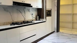 A modern kitchen with white cabinets, a gas stove, and a marble floor. - Jayz Shortlet Apartment (Abuja)