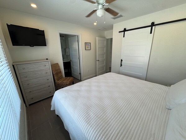 Un dormitorio con cama, cómoda, silla, televisor y armario con puerta corrediza.