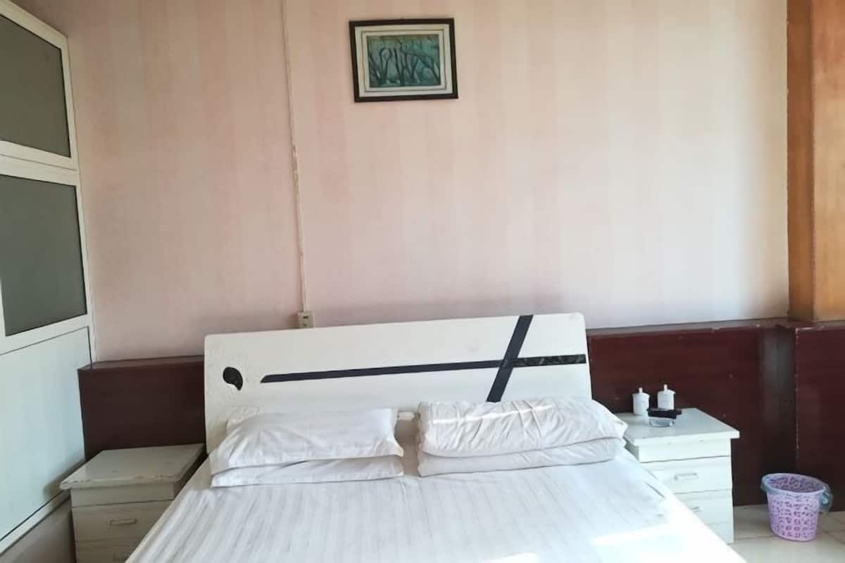 A bed with white bedding, a nightstand with a lamp, and a small trash bin.