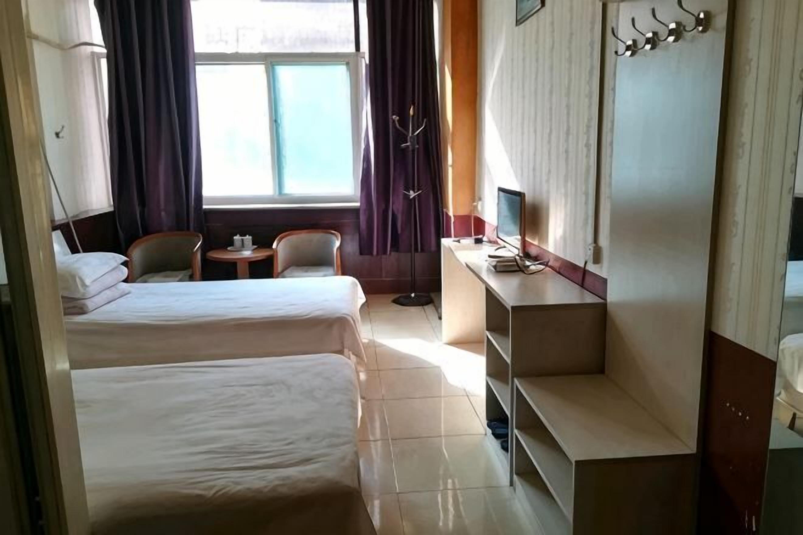 Habitación de hotel con dos camas, un escritorio con computadora, una silla, una mesita y una ventana con cortinas.