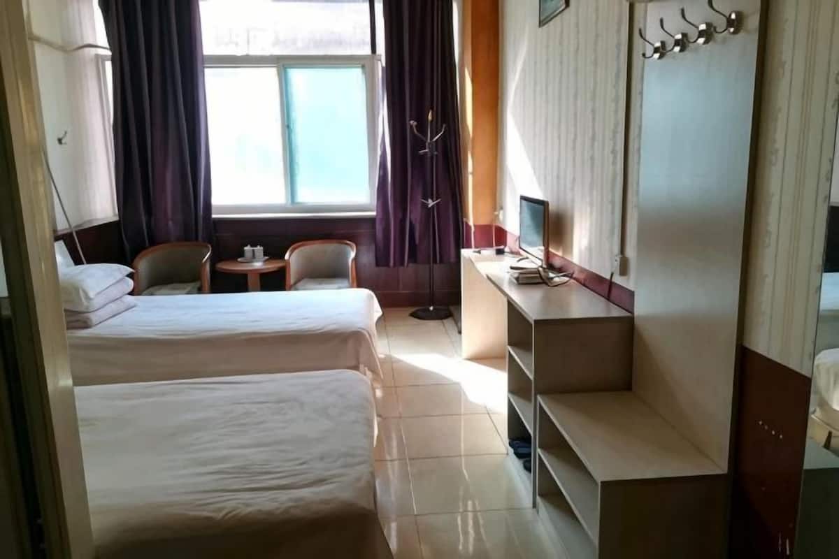 A hotel room with two beds, a desk with a computer, a chair, a small table, and a window with curtains.