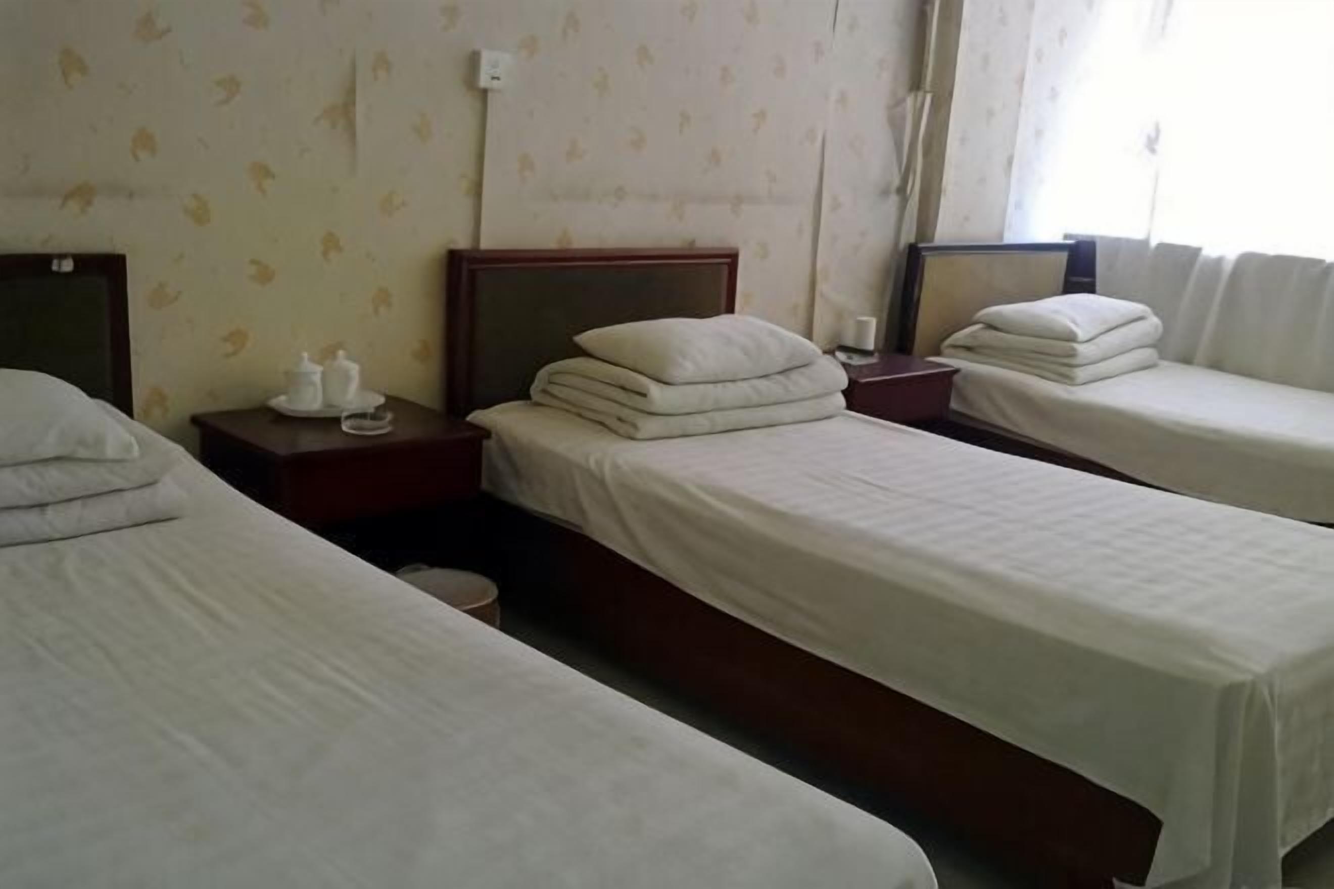Habitación de hotel con dos camas individuales, una mesita de noche con lámpara y una ventana con cortinas.