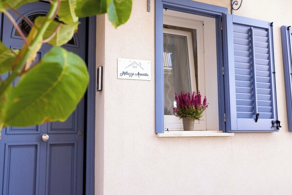 Una casa con una puerta azul y una ventana con contraventanas azules. Hay un letrero en la pared que dice "Muzio Annarita".