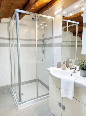 Un baño moderno con ducha envuelta en vidrio, un lavamanos blanco con espejo y techo de madera.