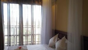 A hotel room with a bed, curtains, and a window with a view. - Rockwell Hotel (Kisumu)