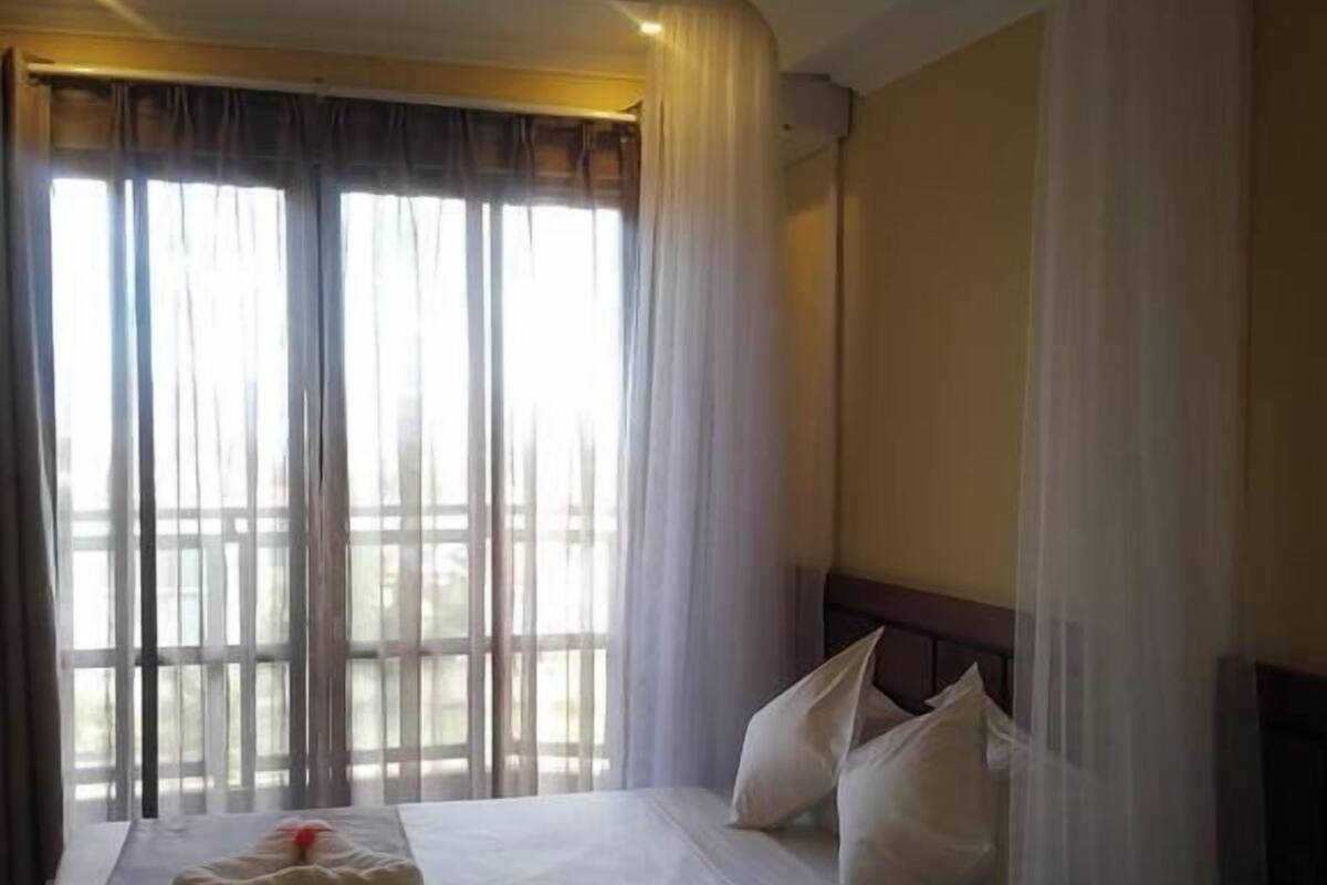 A hotel room with a bed, curtains, and a window with a view.