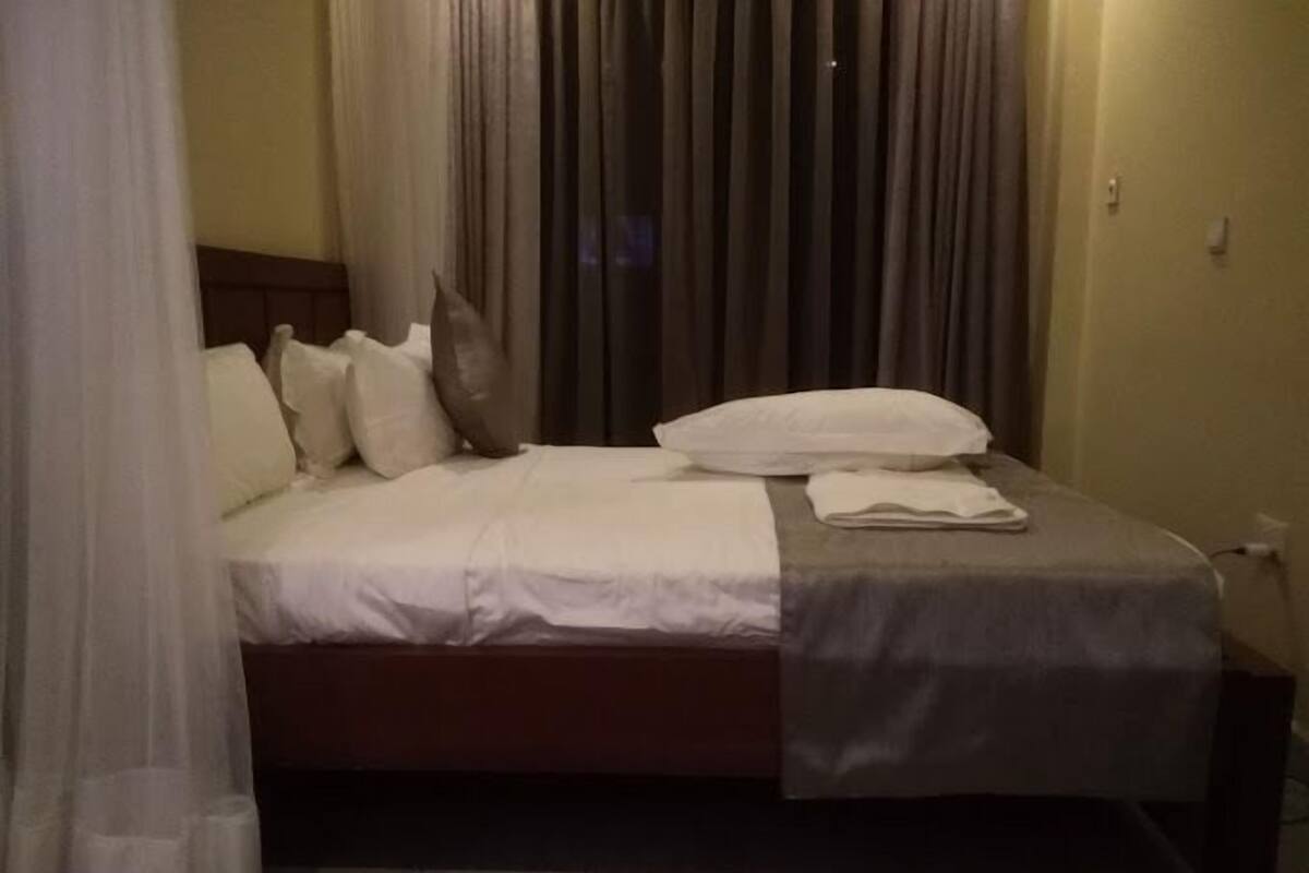 A neatly made bed with white and grey bedding, a wooden headboard, and a bedside table with a lamp.
